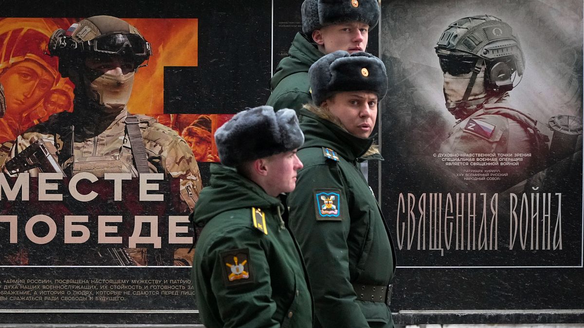 A military patrol passes by a street exhibition of military posters named
