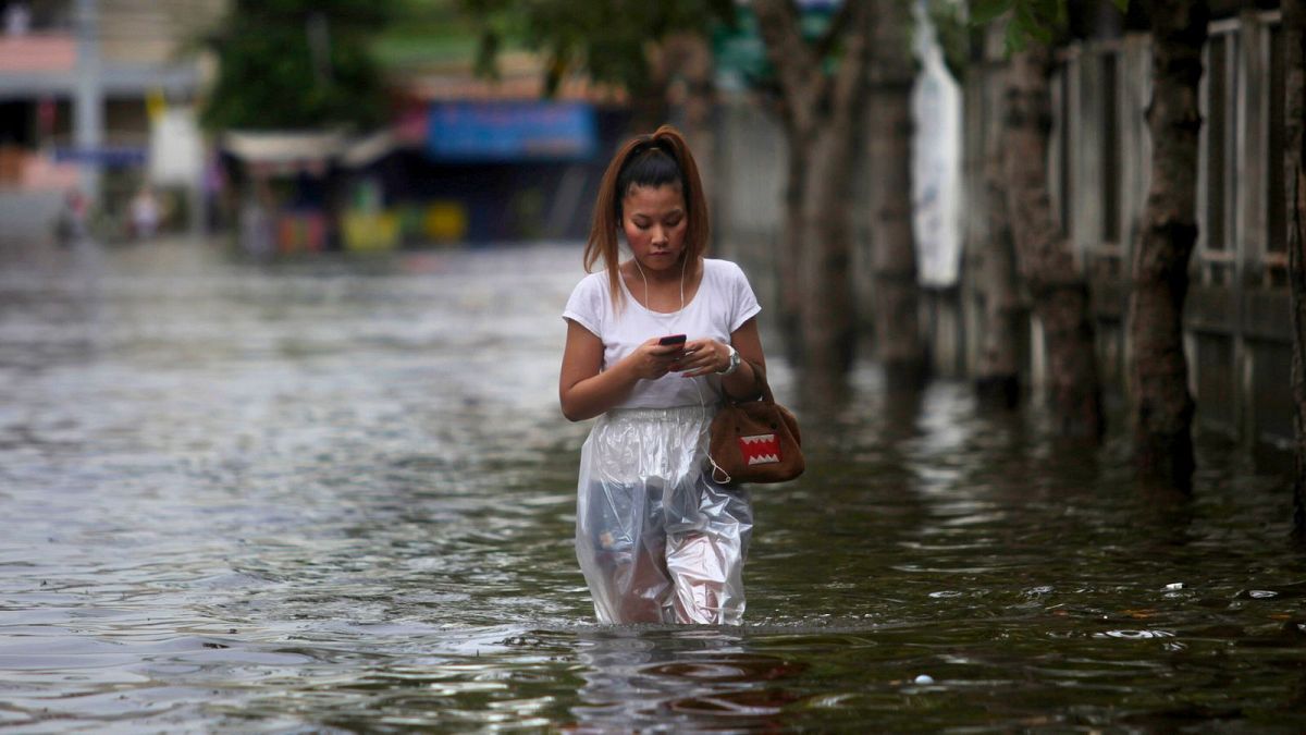 A Thai woman is busy with her mobile phone as she wades through floodwaters on the outskirts of Bangkok, Thailand, Monday, 28 November 2011.