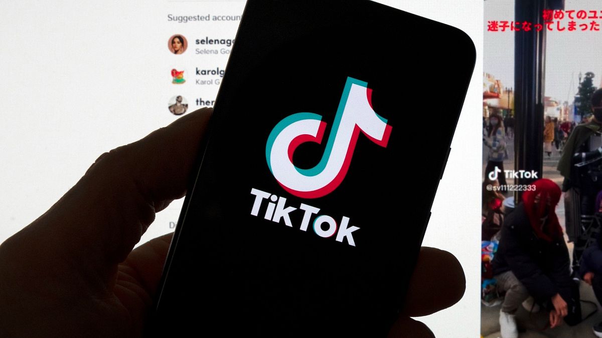 The TikTok logo is seen on a mobile phone in front of a computer screen which displays the TikTok home screen, Saturday, March 18, 2023, in Boston.