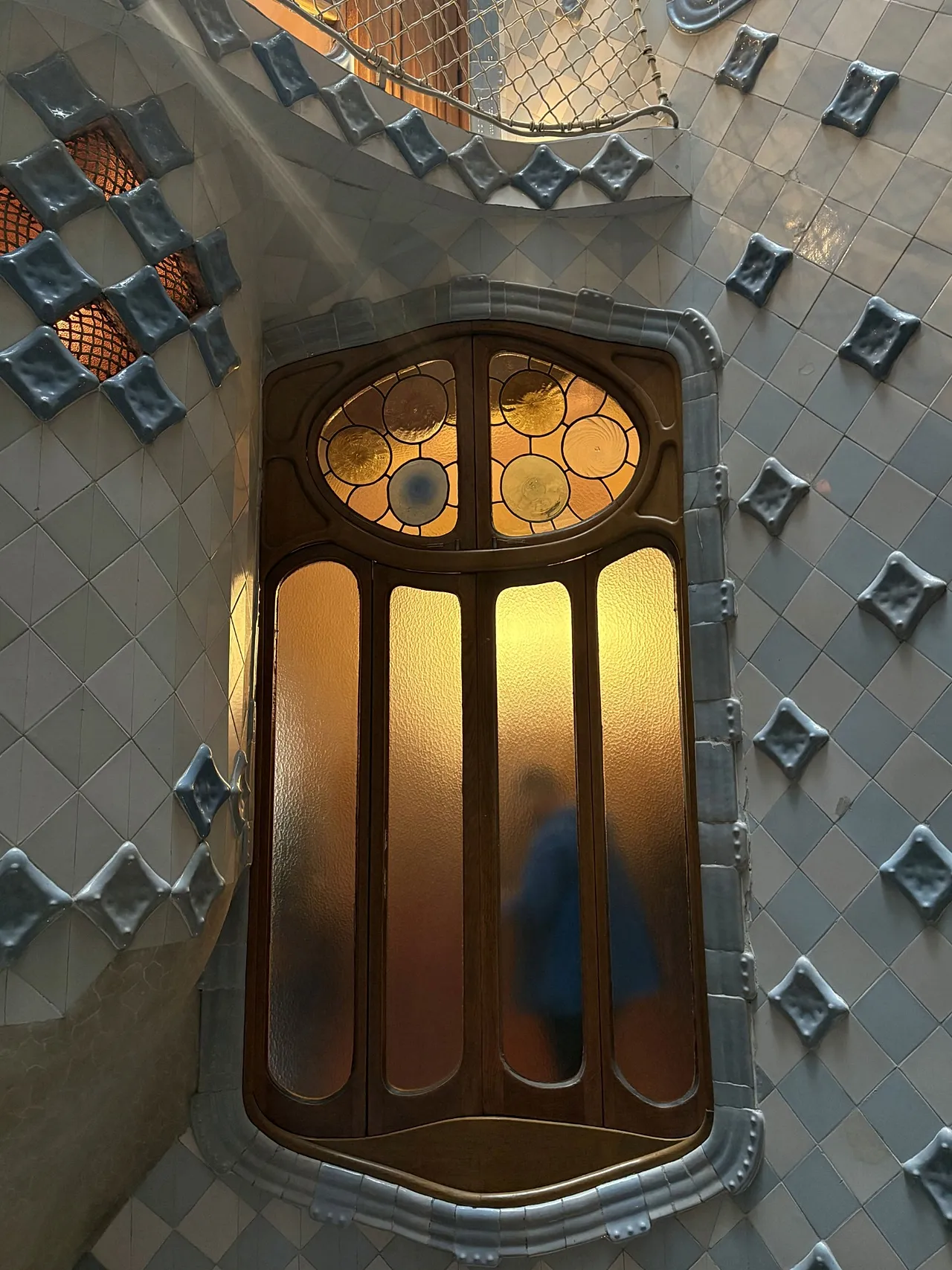 Figur steht hinter einem Fenster mit Blick auf den zentralen Lichtschacht in Casa Batllo, Barcelona, ​​Katalonien, Spanien, 2026.