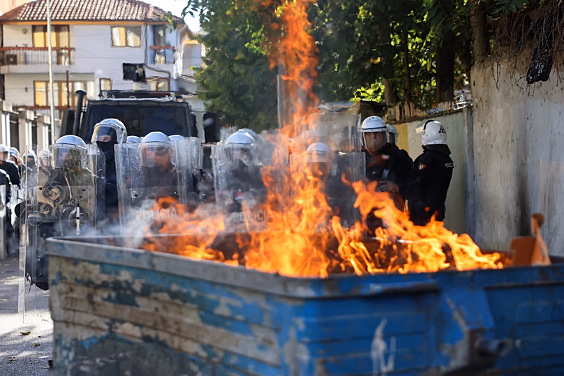 Bereitschaftspolizisten stehen während einer regierungsfeindlichen Kundgebung in Tirana, Albanien, am Samstag, den 24. Oktober 2026, hinter einer brennenden Mülltonne in Formation. (AP Photo/Hameraldi Agolli)
